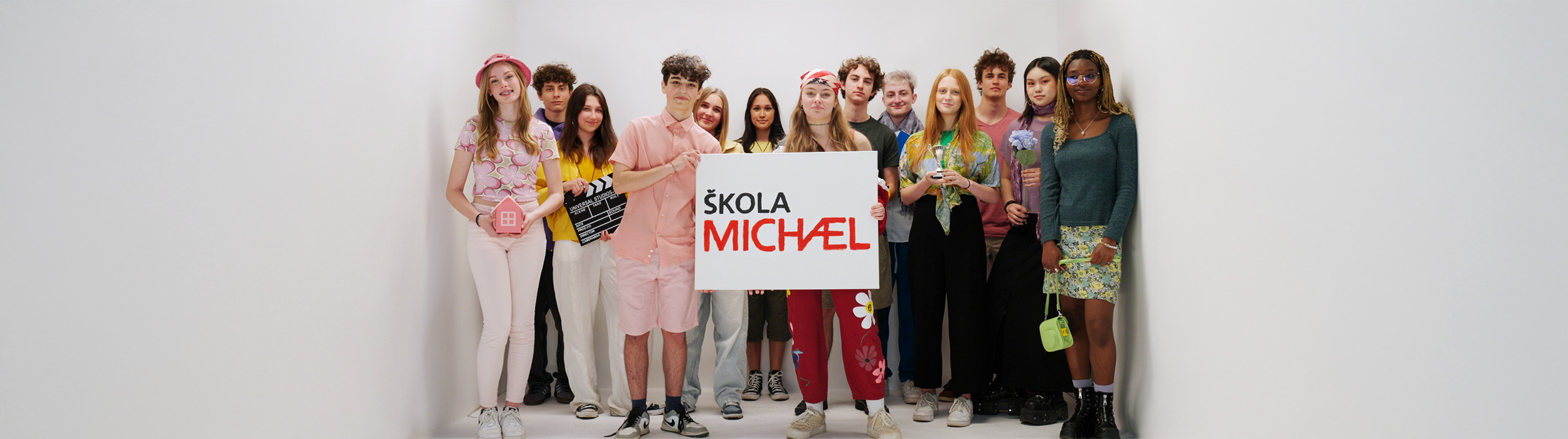 A group of students standing in a white room holding the Škola Michael logo